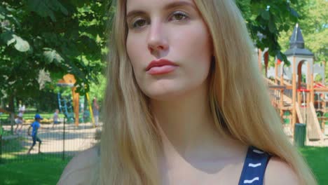 Young-woman-stands-in-front-of-a-children's-playground-looking-seriously-concerned