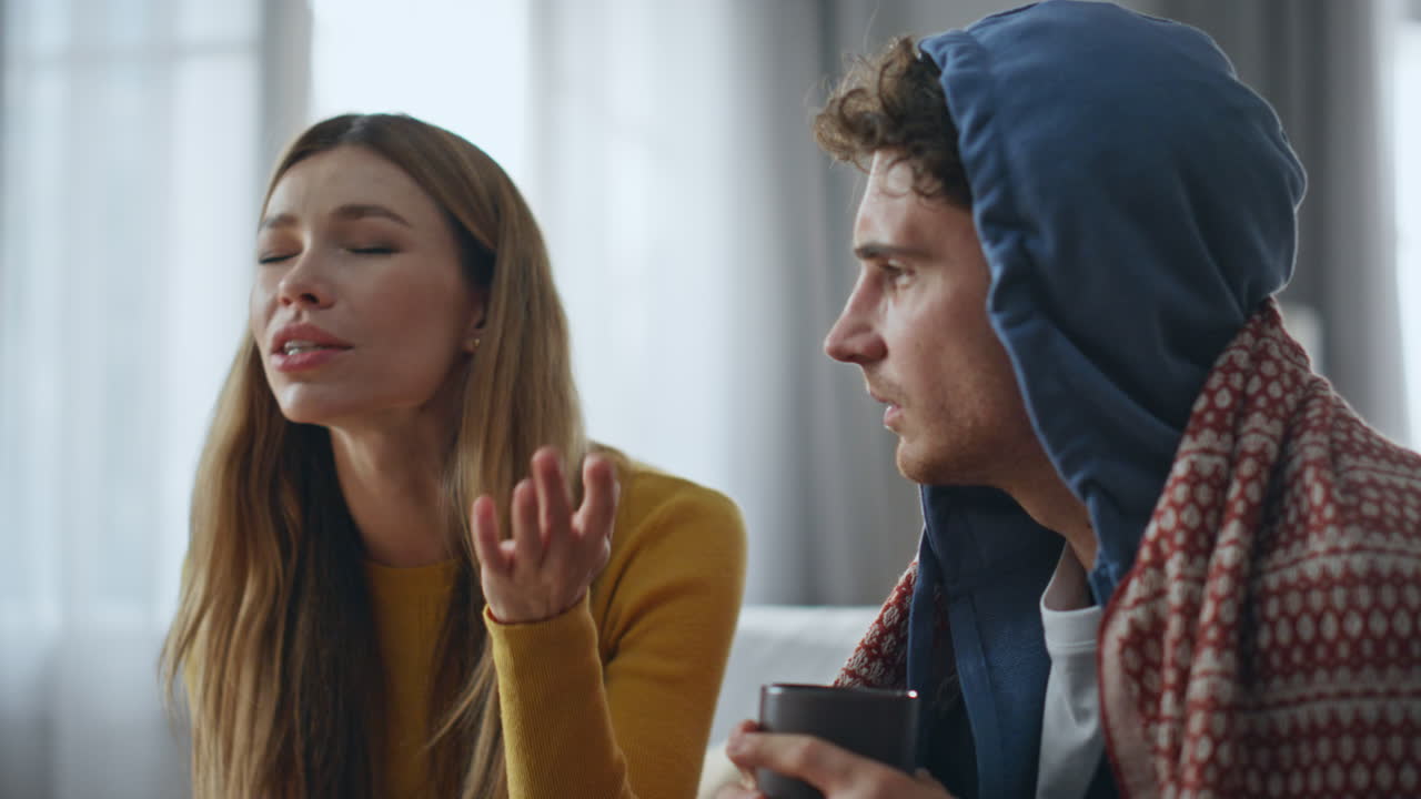 Smiling woman talking sick boyfriend at sofa closeup. Il man drinking hot tea