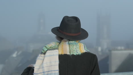 woman in hat looking at city church towers in misty morning