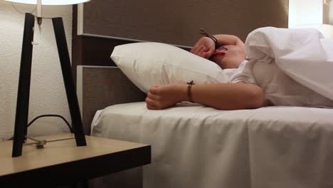 young woman tossing and turning in bed to find comfortable sleep position with lights on