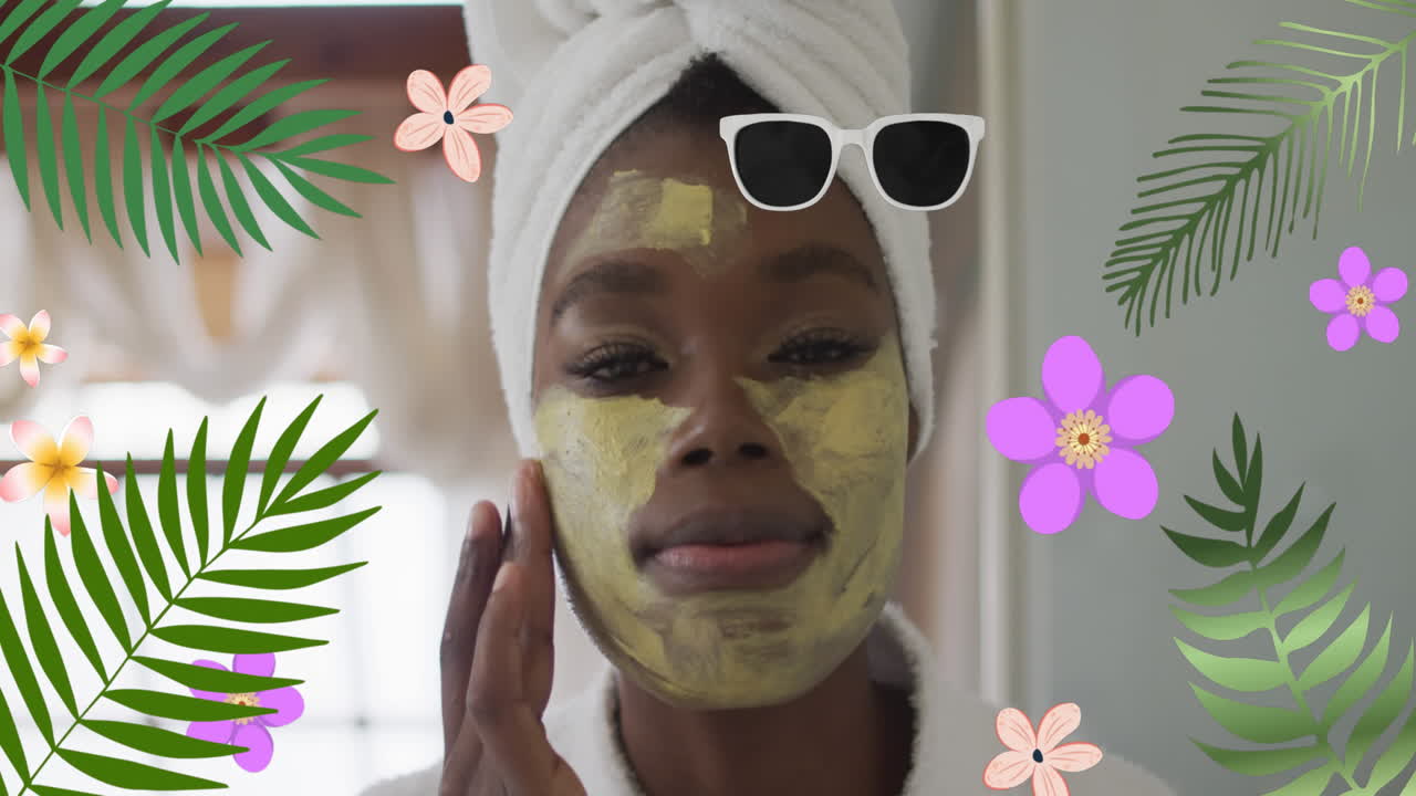 animación de flores sobre una feliz mujer afroamericana aplicando una máscara facial