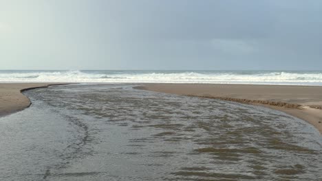 Land-waters-flow-towards-the-sea,-converging-with-it-through-a-channel-on-the-beach,-symbolizing-the-merging-of-land-and-sea-waters,-situated-in-Zahara,-Spain