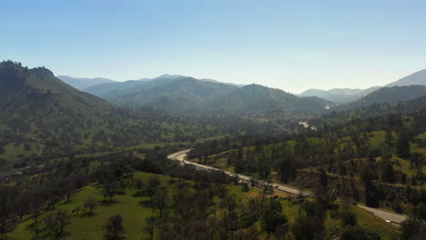 Vista-Aérea-Del-Tráfico-De-La-Carretera-Que-Fluye-A-Través-De-Un-Valle-En-Las-Montañas-Tehachapi-Durante-La-Primavera