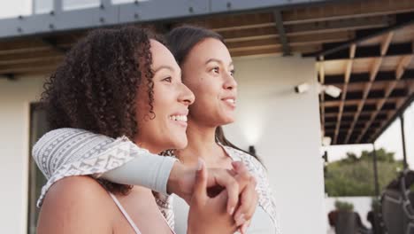 happy biracial lesbian couple embracing and admiring view in garden outside house, slow motion
