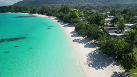 A-drone-flies-over-a-stunning-white-sand-beach-with-a-red-boat-at-Port-Olry-on-the-island-of-Espiritu-Santo