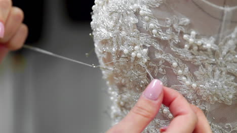 Close-up-fashion-designer-for-brides-in-his-Studio-pins-needles-lace-wedding-dress.-Seamstress-creates-an-exclusive-wedding-dress.-Secure-with-pins-and-needles-outline.-Small-private-business.-Sew-rhinestones-and-crystals-to-the-dress-thread-and-needle.-Jewelry-work.