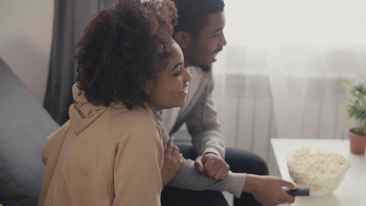 Young Couple Laughing While Watching A Programme On Tv