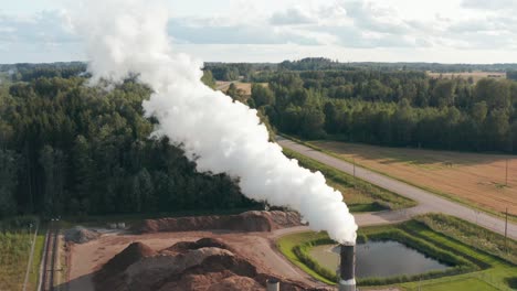 Aerial-drone-shot-of-a-lone-factory-chimney-spewing-fumes-into-atmosphere-in-rural-area