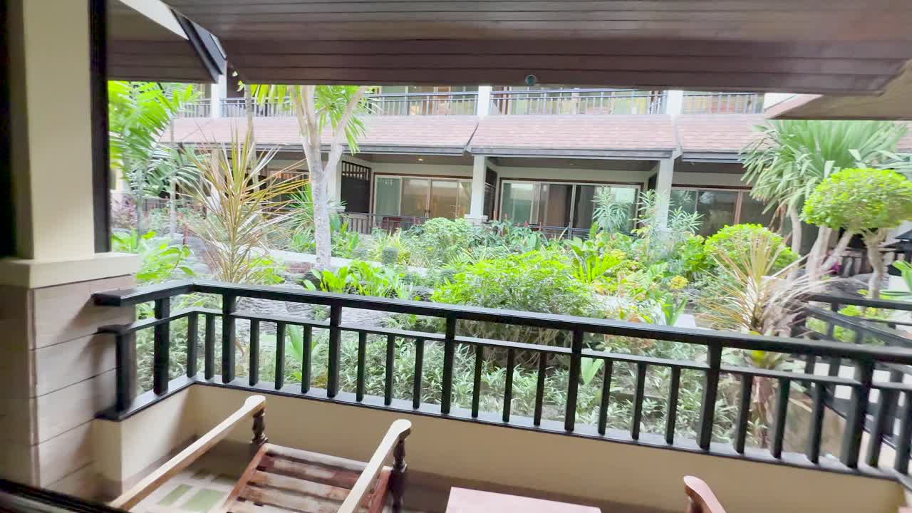 La telecamera si sposta dall'interno di una camera d'hotel a un balcone con vista su un lussureggiante giardino tropicale