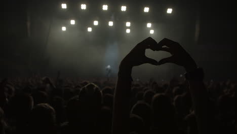person-showing-a-heart-with-hands-on-a-live-concert