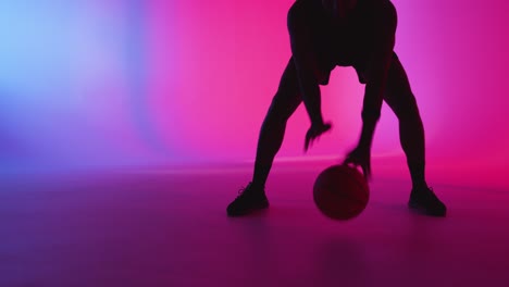 Studiosilhouette-Eines-Männlichen-Basketballspielers,-Der-Den-Ball-Vor-Rosa-Und-Blau-Beleuchtetem-Hintergrund-Dribbelt-Und-Hüpft-1