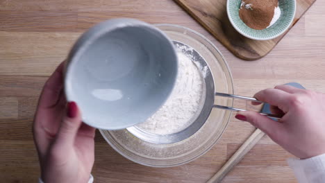 girl sifting flour on fine mesh strainer falling into baking bowl for carrot cake