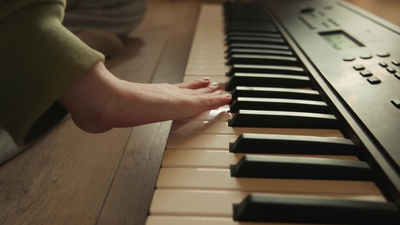 Low-angle close-up showing hands and fingers pressing, sliding, and lifting across electronic piano keys, capturing chord changes, rhythmic touch, and smooth musical movement in warm indoor light