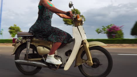 cámara lenta, modelo rubia de moda montando ciclomotor blanco en carretera abierta durante las vacaciones de verano