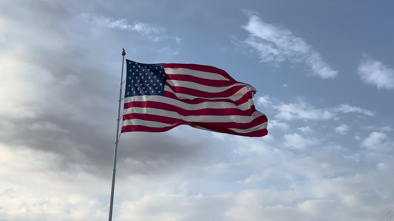 gran bandera estadounidense soplando en el viento contra un cielo azul soleado y nubes blancas a finales de la tarde