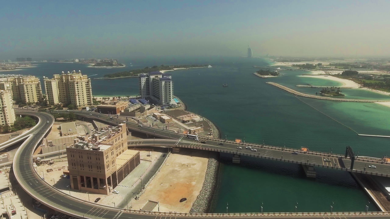 Drone ascending above Dubai Marina showing coastal roads, bridges, turquoise water and modern city skyline