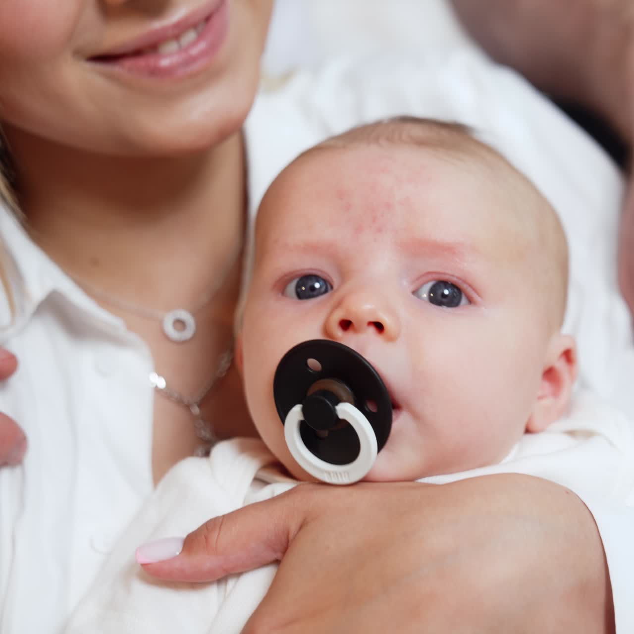 Face of a tiny Caucasian newborn boy with a pacifier in mouth. Baby is dandled in mom's hands