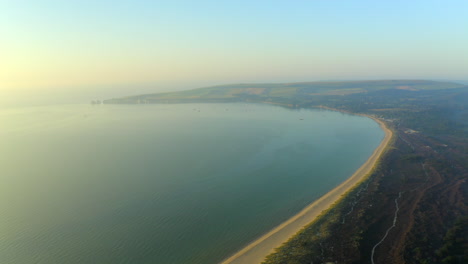 Una-Hermosa-Toma-Aérea-De-La-Bahía-Y-La-Playa-De-Studland-Con-Rocas-Antiguas-De-Harry-En-El-Fondo-A-La-Hora-Dorada-En-El-Verano