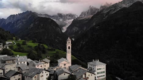 aerial flyover over the rooftops of the historical village of soglio in the bregaglia region of grissons, switzerland with a view of the old church and mountain peaks of engadin