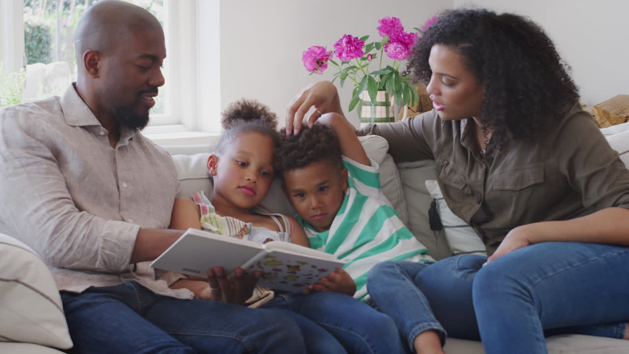 Genitori seduti sul divano a casa con i figli che leggono un libro insieme.