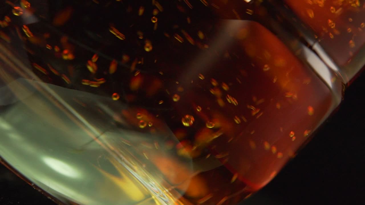 Versare whisky in un bicchiere trasparente, sfondo nero - Primo piano.