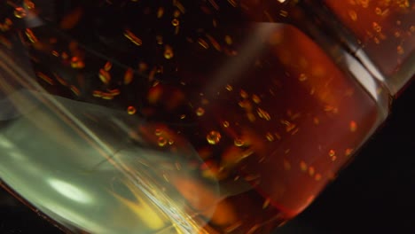 pouring whisky into clear glass, black background - close up