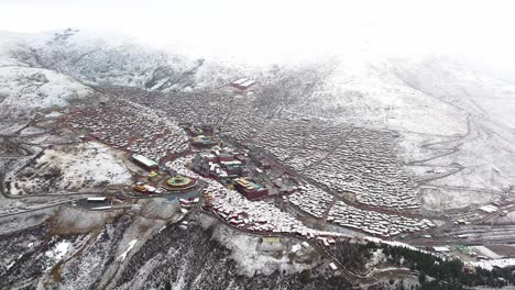 Aerial-establishing-overview-of-Larung-Gar-Tibetan-Buddhist-academy-and-town-covered-in-snow,-TIbet,-China