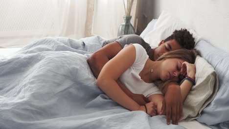 Multiracial-couple-lying-in-bed-and-sleeping-while-embracing-each-other.-Young-family-concept