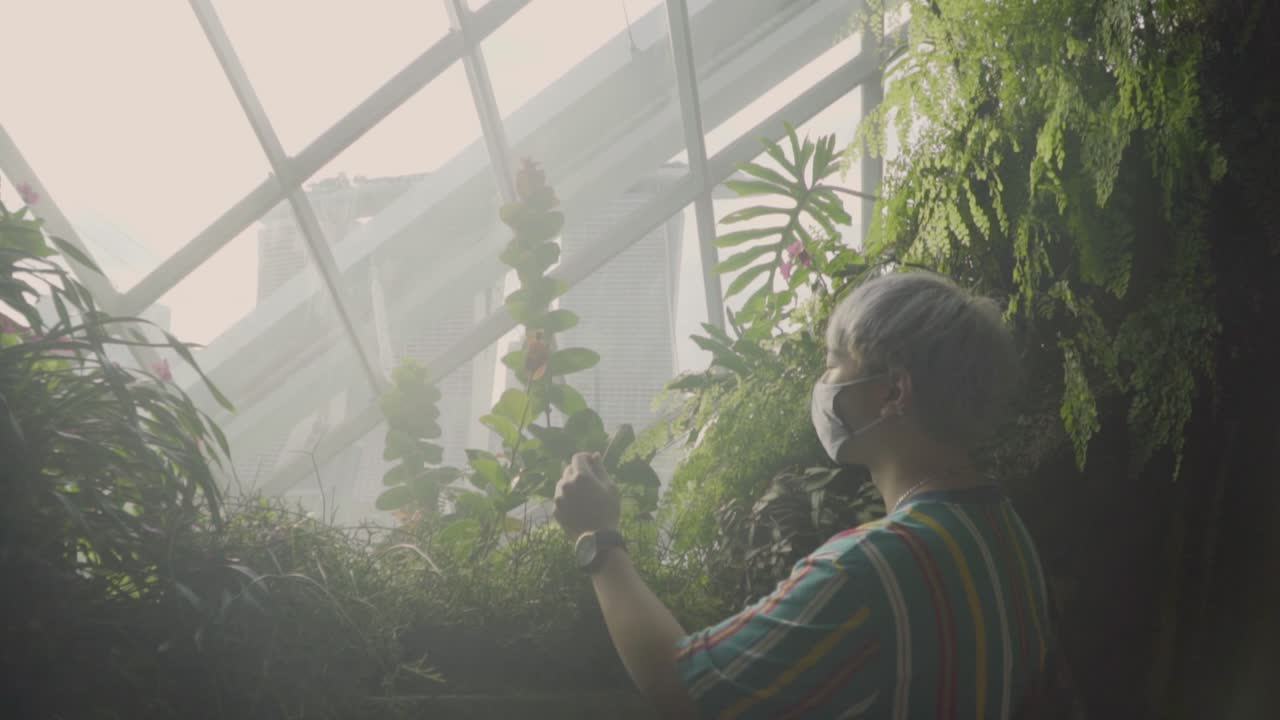 Young Man Wearing Face Mask Enjoying The View Of Marina Bay Sands From Cloud Forest In Singapore. - dolly shot