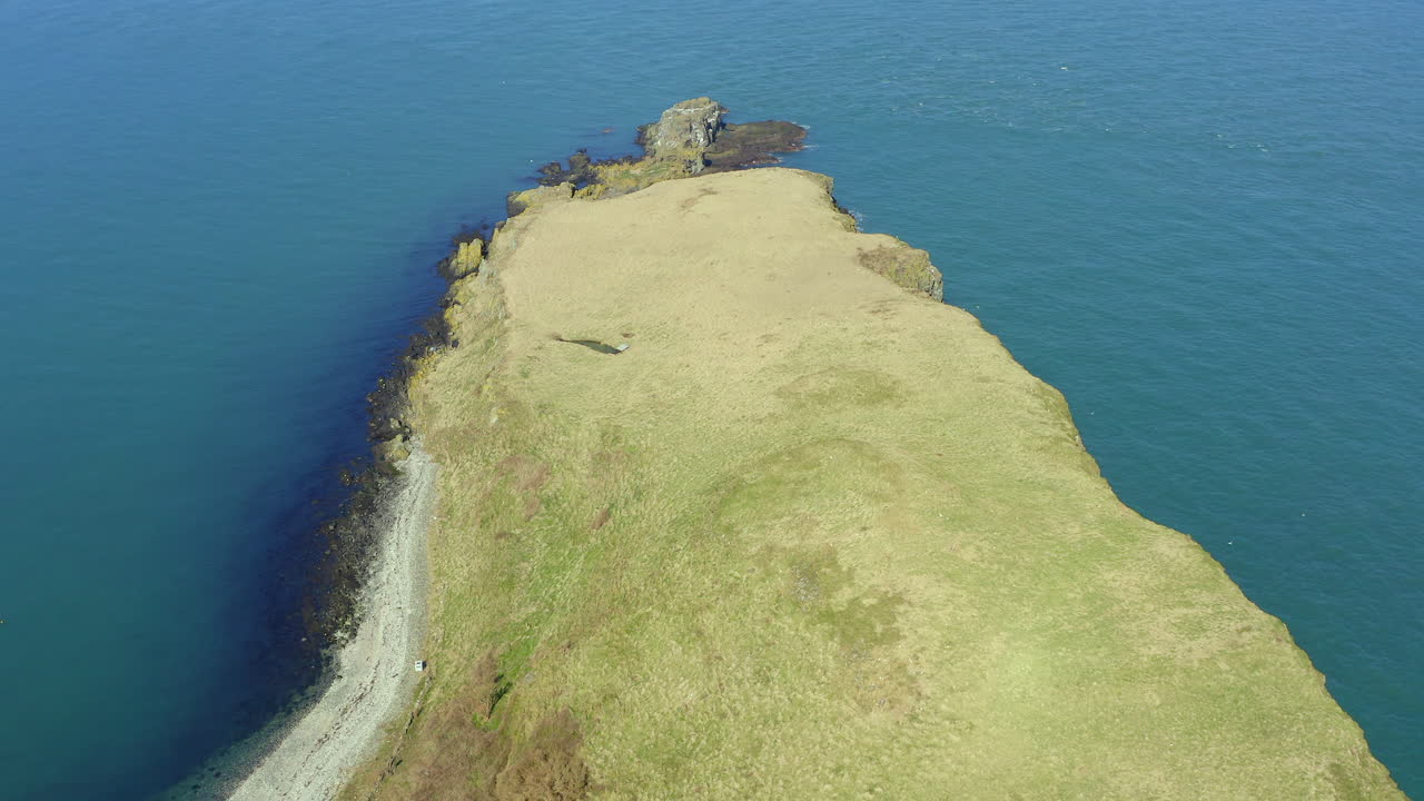 Aerial drone pullback revealing the full expanse of Portmurk island, capturing its rugged contours against Northern Ireland's coastal waters