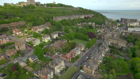 drone footage showcasing a residential area in dover with houses, green spaces, a historic castle on a hill, and the coastline in the background