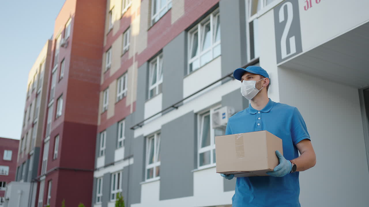 An young mailman courier with a protective mask and gloves is delivering a parcel directly to a customer home with safety. Concept of courier home delivery e-commerce shipping virus covid