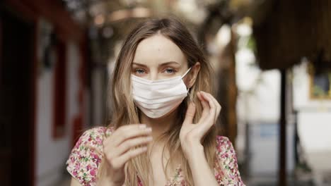 mujer rubia poniendo una máscara médica para la protección contra el coronavirus al aire libre