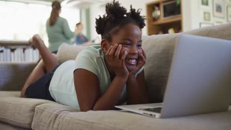 happy african american girl lying on sofa using laptop