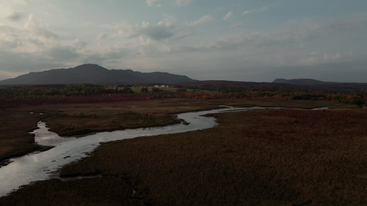 arroyo cours d'eau shonyo junto a los prados con paisaje de montaña en su fondo bajo un cielo nublado en magog, municipios del este, quebec, canadá
