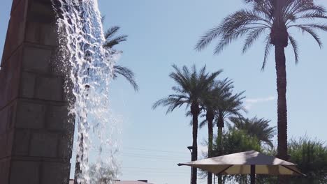 slow-motion tilt-down from the spout of a freestanding water feature, a brick fountain surrounded by palm trees and city streets, scottsdale, arizona