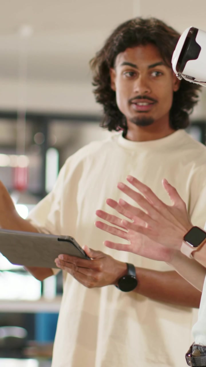 Vertical video: Tapping tech in cream shirt with tablet in lab as peer raising hand, guiding VR