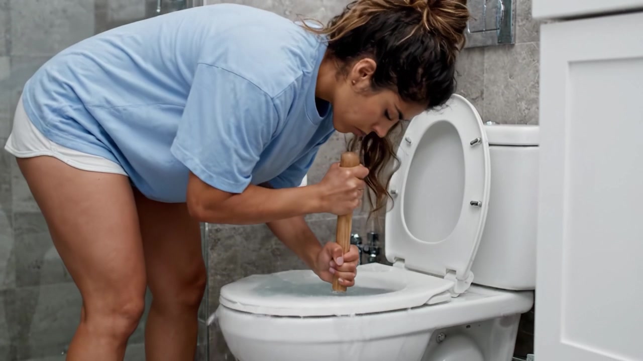 A determined individual addresses a common household issue by using a plunger to unclog a toilet, showcasing a hands-on approach to home maintenance and problem-solving.