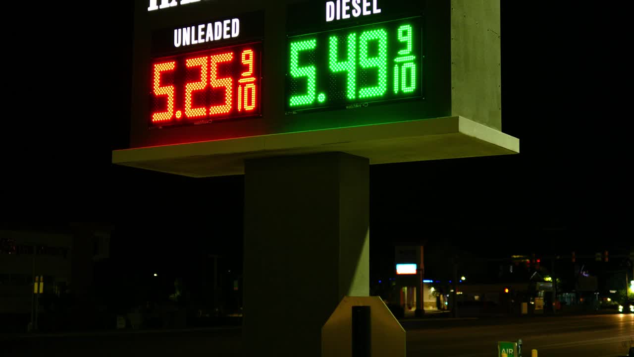 Gas station prices LED light up sign for regular and diesel fuel at night over 5 dollars per gallon credit and cash price, during 2021 2022 war time recession, ground up shot with angle and car