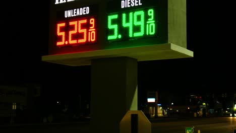 gas station prices led light up sign for regular and diesel fuel at night over 5 dollars per gallon credit and cash price, during 2021 2022 war time recession, ground up shot with angle and car
