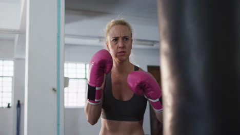 una boxeadora caucásica con guantes de boxeo pateando el saco de boxes en el gimnasio