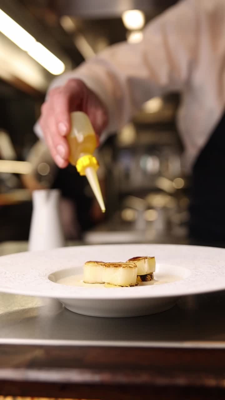 Chef che impiattano capesante con salsa