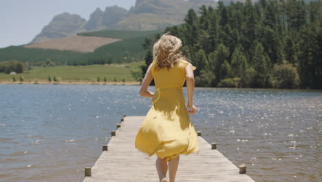 Mujer-Joven-Corriendo-Saltando-Del-Embarcadero-En-El-Lago-Chapoteando-En-El-Agua-Disfrutando-De-La-Libertad-De-Verano