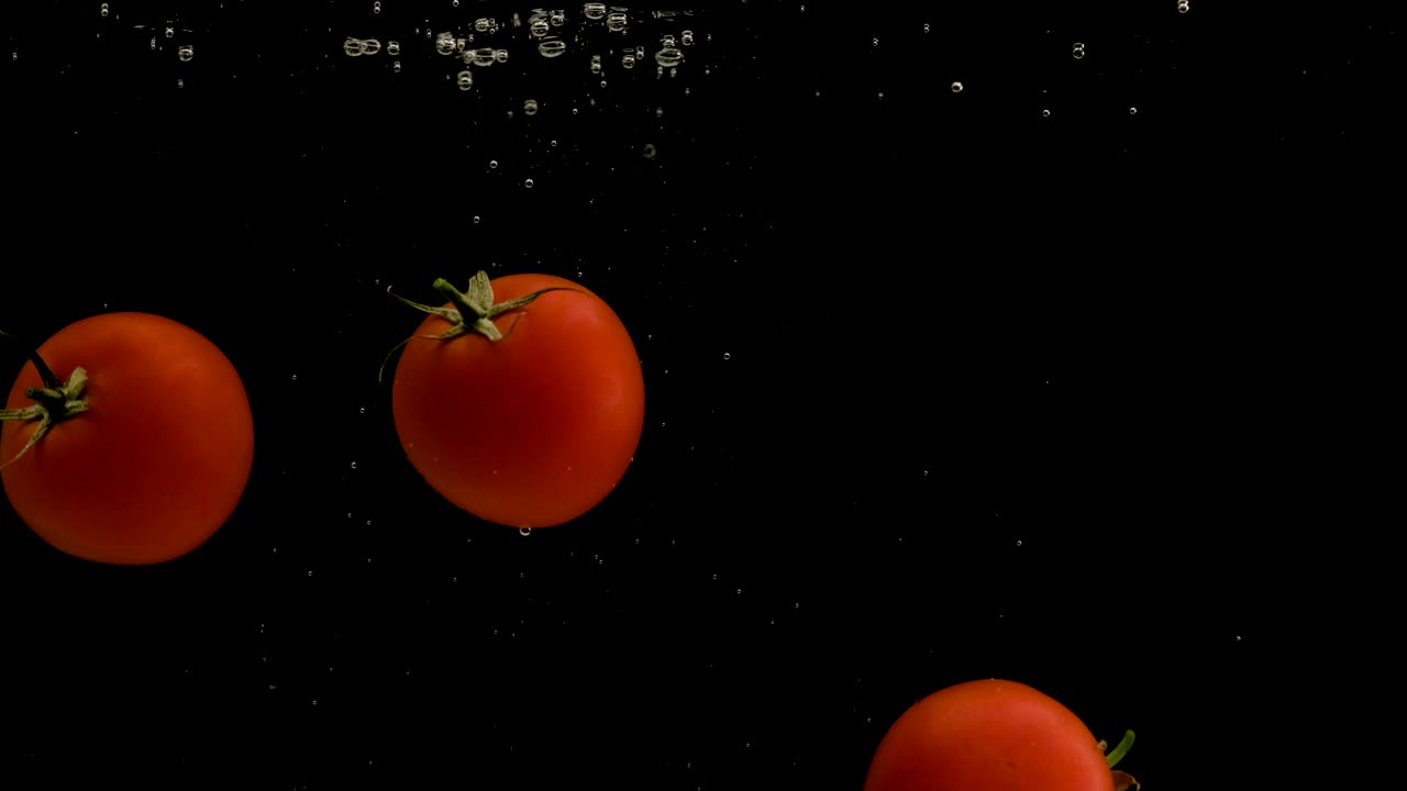 검은 바탕에 물에 떨어지는 토마토. 밝은 고품질 비디오