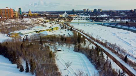 Aerial-Winter-Flyover-Drop-Im-Victoria-Park-Künstliche-Ruhige-Eisbahn,-Die-Mit-Einer-Infinity-Skatebahn-Neben-Der-Schneebedeckten-Forststraße-Am-North-Saskatchewan-River-Am-Royal-Glenora-Club-Downtown-City4-4-Verbunden-Ist