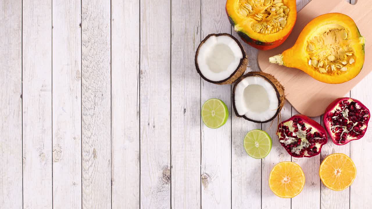 Zucca a fette, cocco, lime, arancia e melograno in movimento su sfondo in legno. Stop motion