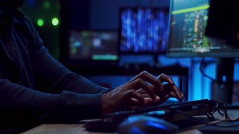 close up of the young male hacker or software developer tapping, typing and texting on the keyboard of computer at night while programming