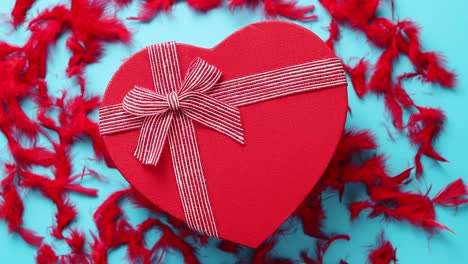 Red--heart-shaped-gift-box-placed-on-blue-background-among-red-feathers