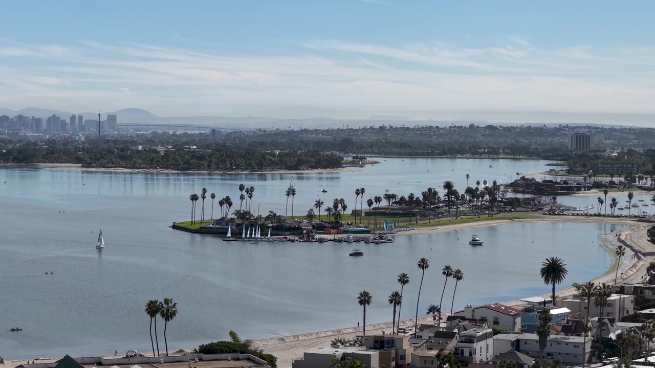 Attività velica a Mission Bay con lo skyline di San Diego visibile all'orizzonte, barche a vela sulle calme acque della baia e lontani edifici del centro, Pacific Beach, California.
