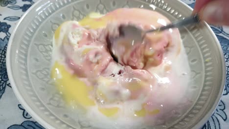 strawberry, vanilla and black current flavored ice cream with yellow vanilla custard topping, delicious sunday dessert being scooped with stainless steel spoon in porcelain bowl